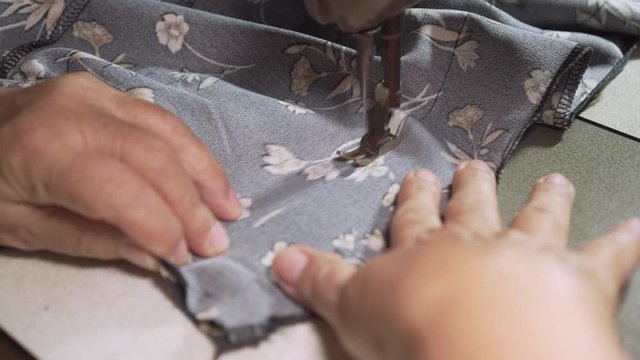 Old asian lady using sewing machine for stitching fabric with flower pattern.  Close up