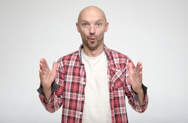 Shocked bald man showing huge size gesture with hands and looks in surprise with big eyes at the camera.