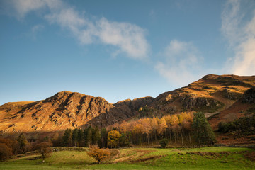 Majestic vibrant Autumn Fall landscape Buttermere in Lake District with beautiful early morning sunlight playing across the hills and mountains