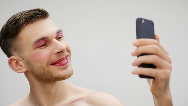 Handsome travesty man making selfie on smartphone. Transsexual with makeup doing photo on phone. Transsexual concept. Gay with travesty makeup looking at smartphone