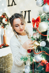 Beautiful young girl with two braids dresses up the Christmas tree close up