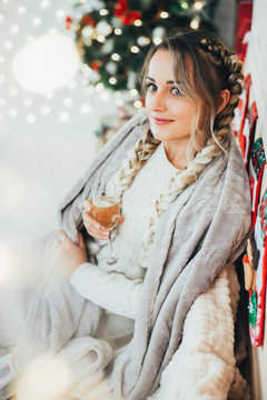 cute girl on the background of the Christmas tree sitting with a glass of champagne or wine wrapped in a blanket