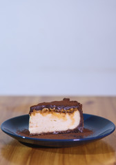 Snickers cheesecake on a blue saucer on a large bright wooden table
