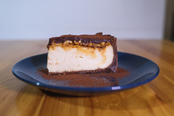 Snickers cheesecake on a blue saucer on a large bright wooden table