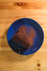 Snickers cheesecake on a blue saucer on a large bright wooden table