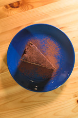 Snickers cheesecake on a blue saucer on a large bright wooden table