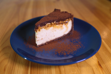 Snickers cheesecake on a blue saucer on a large bright wooden table