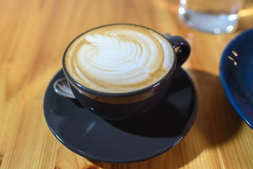 Snickers cheesecake on a blue saucer, a glass of water and a cup of fresh cappuccino on a large bright wooden table