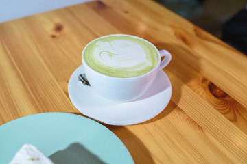 Matcha latte and pistachio cheesecake on a large bright wooden table