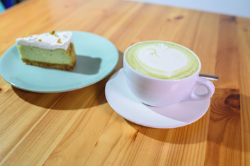 Matcha latte and pistachio cheesecake on a large bright wooden table