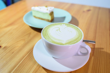 Matcha latte and pistachio cheesecake on a large bright wooden table