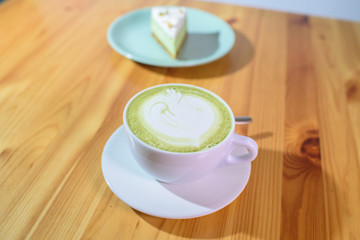 Matcha latte and pistachio cheesecake on a large bright wooden table