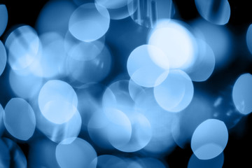 Seasonal bluured background of Christmas lights on the tree toned in classic blue. Celebration concept. Soft focus. Horizontal