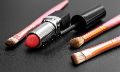 Makeup brushes with lipstick and mascara brush on black.