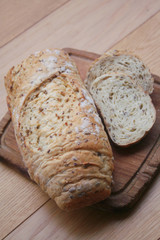 Partially sliced wholegrain organic bread with different seeds on a wooden cutting board on table