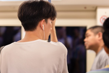 Asian man passenger listening music via smart mobile phone in subway train.