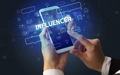 Female hand typing on smartphone with INFLUENCER inscription, social media concept