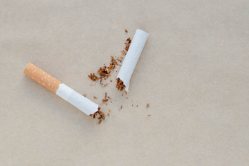 A broken cigarette on a light brown paper background. Scattered tobacco. Copy, text space. Bad habit. Say no to addiction. Healthy lifestyle concept.