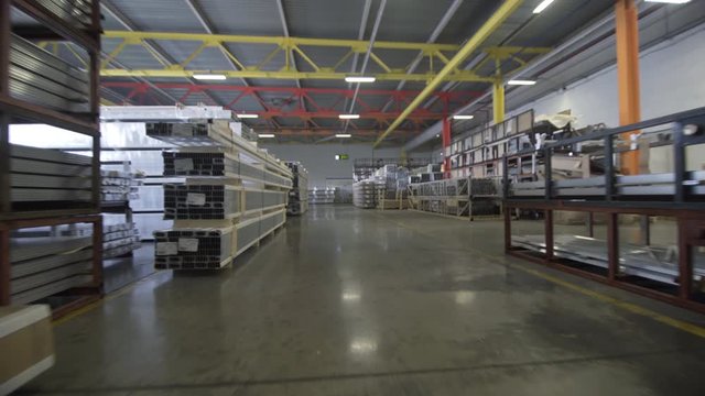 Racks with window profiles in a warehouse. The camera moves along racks. Profiles in cardboard package, a part are not up to the end unpacked. It is visible a warehouse roof. There are no people near
