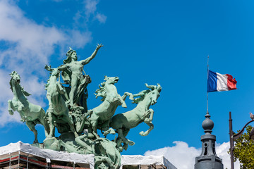 Obraz premium The L'Harmonie Triomphant de la Discorde statue and French National flag on the Grand Palais in Paris