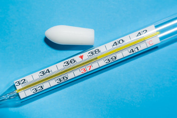 White suppository for anal or vaginal use on blue background and a thermometer with temperature of...