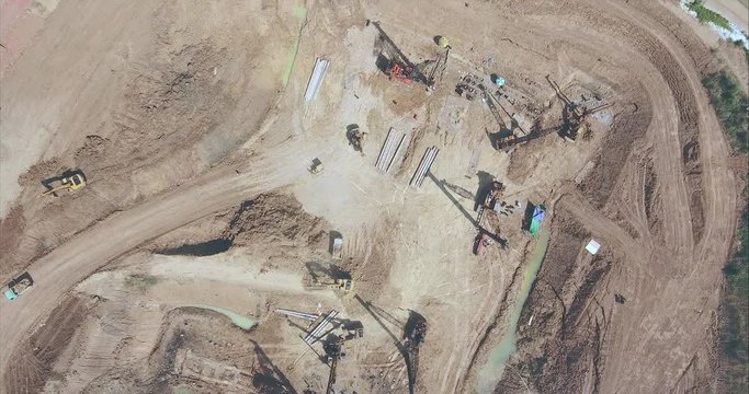 drone shot looking down at the the  construction site. Drilling piles with heavy machinery and excavator loading sand into a small truck 