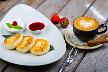 Traditional breakfast with coffee and cheesecakes, cottage cheese pancakes on a plate with syrup and jam.