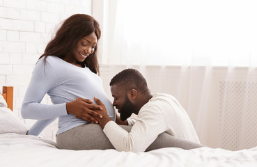 Blissful man kissing his happy pregnant wife belly