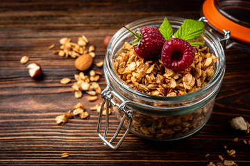 Granola in glass jar and raspberry on dark wooden background.