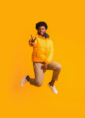 Fototapeta na wymiar Positive winter black guy greeting with peace gesture while jumping