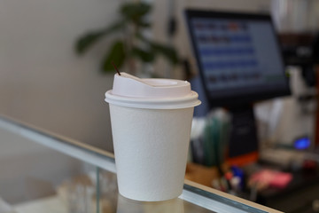 Disposable coffee cup made with paper. White Paper coffee cup on glass table in front of Blur cashier background. Selective Focus.