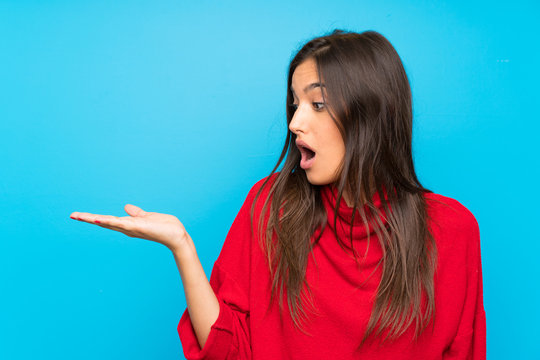 Young woman with red sweater over isolated blue background holding copyspace imaginary on the palm