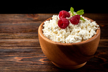 Cottage cheese with raspberry in wooden bowl on dark wooden background.