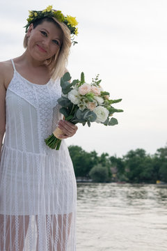 beautiful bride with wedding bouquet standing on a boat and posing for the photographer near the river