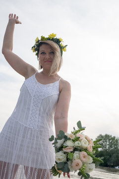 beautiful bride with wedding bouquet standing on a boat and posing for the photographer near the river