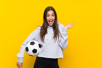 Young football player woman over isolated yellow background with shocked facial expression