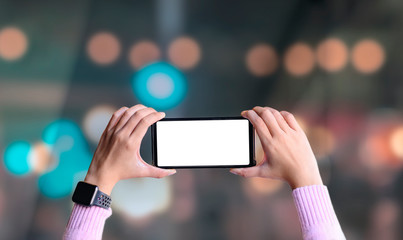 Close-up of female hand holding horizontal blank screen smart phone with blurred bokeh background.