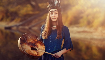 beautiful shamanic girl playing on shaman frame drum in the nature.