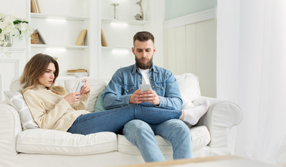 Internet addiction. Young couple using smartphones on sofa