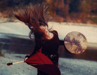 beautiful shamanic girl playing on shaman frame drum in the nature and light graphic effect.