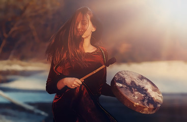 beautiful shamanic girl playing on shaman frame drum in the nature and light graphic effect.