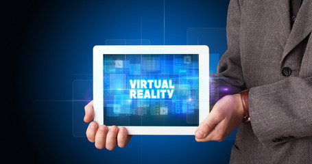 Young business person working on tablet and shows the inscription: VIRTUAL REALITY