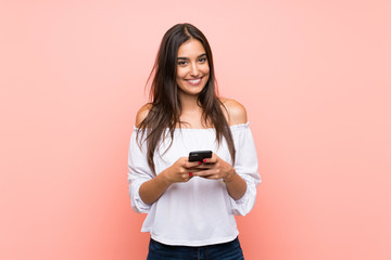 Young woman over isolated pink background sending a message with the mobile