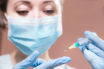 A professional cosmetologist doctor holds in his hand a syringe with anti-aging fluid. A hanging drop on the end of a needle with a filler over a gloved doctor finger.