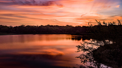 Naklejka premium Golden hour sunset over a pond with clouds and sky silhouetting the trees