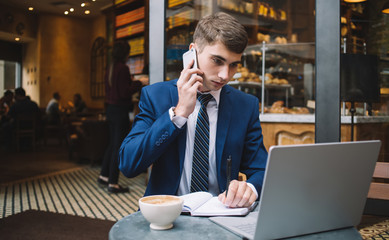 Contemporary businessman calling by phone while working in cafe