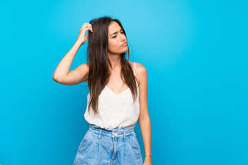 Young woman over isolated blue background having doubts while scratching head