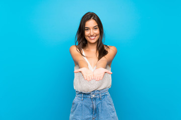 Young woman over isolated blue background holding copyspace imaginary on the palm to insert an ad