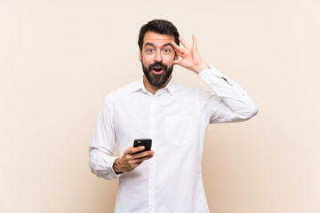 Young man with beard holding a mobile with surprise expression