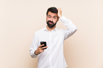 Young man with beard holding a mobile with an expression of frustration and not understanding